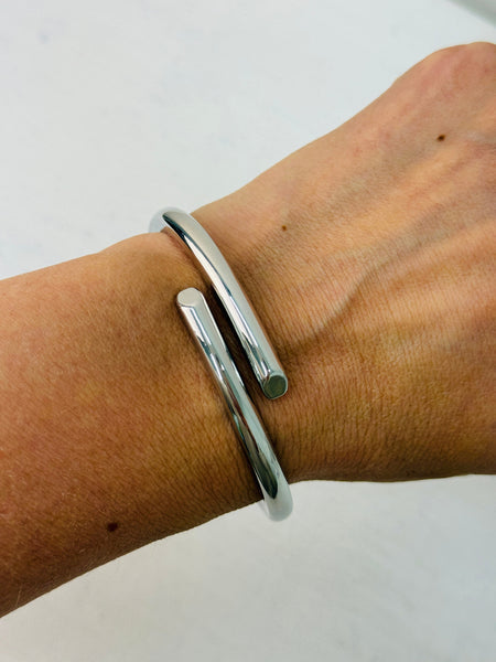 A sleek silver bracelet with a modern open-ended design, displayed on a model.
