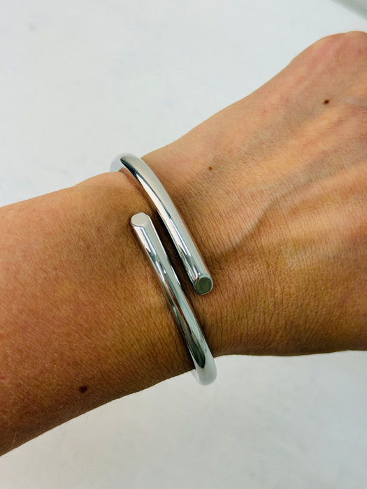 A sleek silver bracelet with a modern open-ended design, displayed on a model.