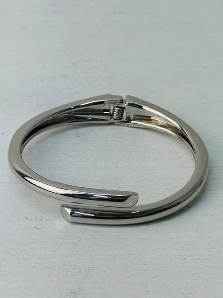 A sleek silver bracelet with a modern open-ended design, displayed on a white background.