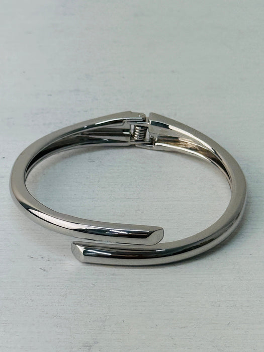 A sleek silver bracelet with a modern open-ended design, displayed on a white background.