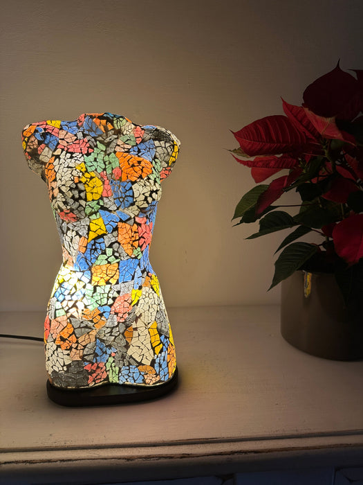 Bust-shaped mosaic lamp glowing warmly in low-light setting.