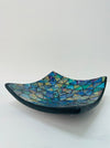 Side view of handmade small mosaic square plate showing curved terracotta base and shimmering blue glass surface.