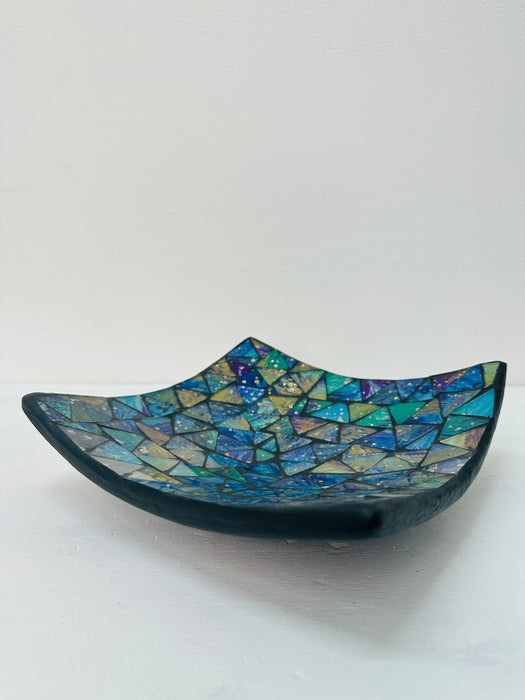 Side view of handmade small mosaic square plate showing curved terracotta base and shimmering blue glass surface.