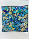 Top view of handmade small mosaic square plate showing geometric cyan and blue glass pieces arranged in pattern.