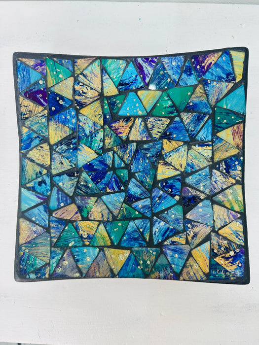 Top view of handmade small mosaic square plate showing geometric cyan and blue glass pieces arranged in pattern.