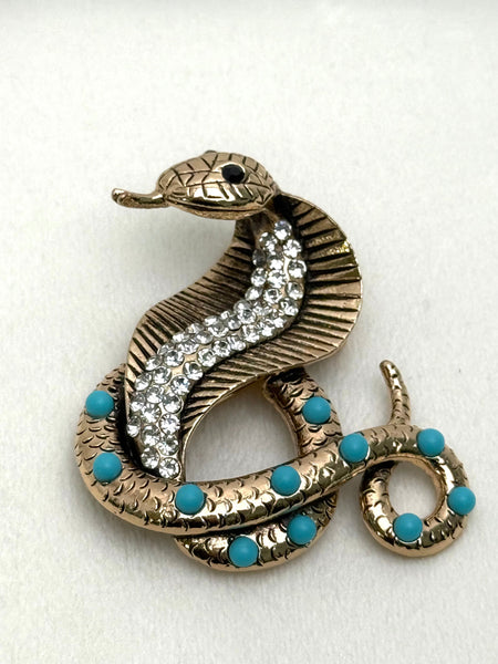 Gold snake-shaped brooch with turquoise accents on a white background