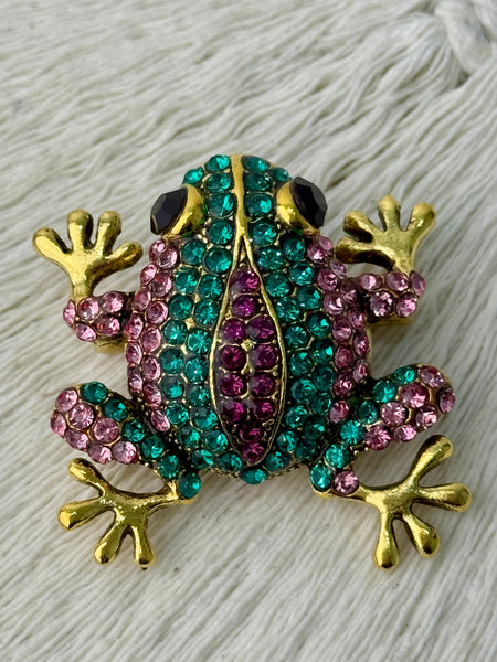 Decorative frog pin with gemstones on a textured surface