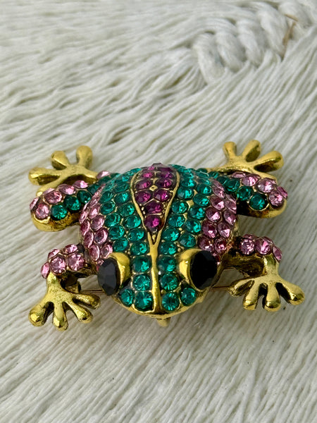 Elegant gold-tone frog brooch with sparkling green and purple crystals.