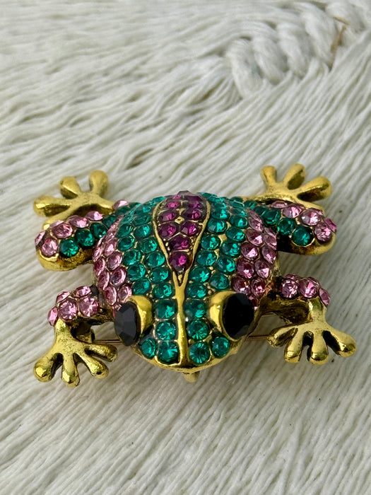 Elegant gold-tone frog brooch with sparkling green and purple crystals.