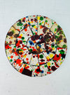 A circular mosaic coaster with a variety of colors splattered across its surface, with a hand-painted appearance.