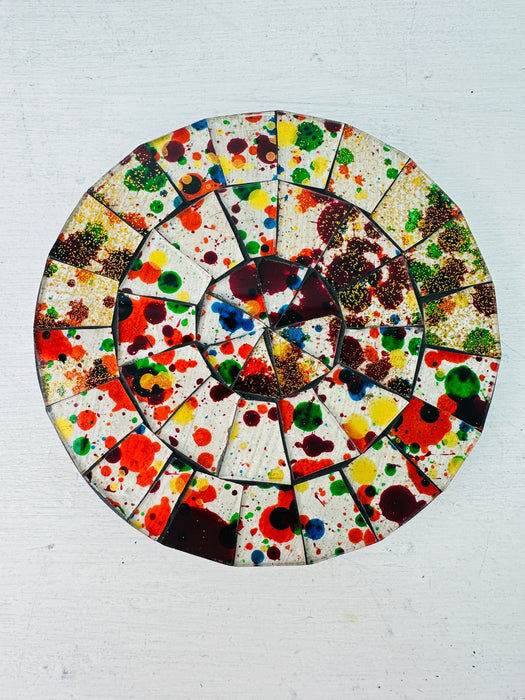 A circular mosaic coaster with a variety of colors splattered across its surface, with a hand-painted appearance.