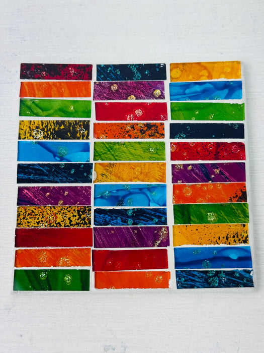 Square Rainbow Brick mosaic coaster with colourful rectangular hand-painted glass pieces arranged on an MDF base, photographed from above on a light surface.