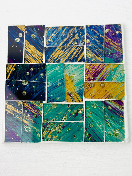 Square Cyan mosaic coaster with hand-painted glass tiles in shades of blue, green and gold arranged on an MDF base, photographed from above on a light surface.