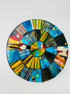 A hand painted round mosaic coaster with a vibrant geometric pattern, featuring colors such as blue, yellow, green, and red.