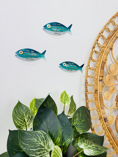 Aqua striped metal fish wall art displayed beside indoor plants and decorative plate