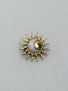 Gold sun-shaped brooch with a central moon on a light gray background