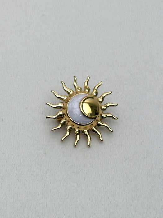 Gold sun-shaped brooch with a central moon on a light gray background