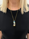 A person wearing a black top and showcasing a gold-colored necklace with a turquoise and blue tea cup pendant.