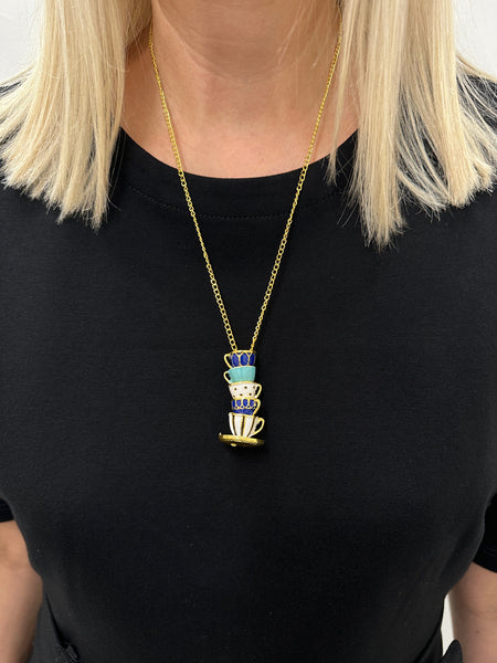 A person wearing a black top and showcasing a gold-colored necklace with a turquoise and blue tea cup pendant.