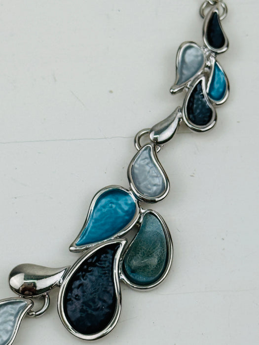 Close-up of turquoise, grey and gunmetal teardrop-shaped enamel necklace with silver-tone chain, largest drop in the centre measures 2cm.