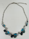 Teardrop enamel necklace in turquoise, grey, gunmetal and silver tones, displayed on a table.