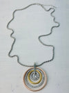 A necklace with three concentric circles in silver, rose gold, and gold colors, featuring a Lobster clasp fastening on a chain.