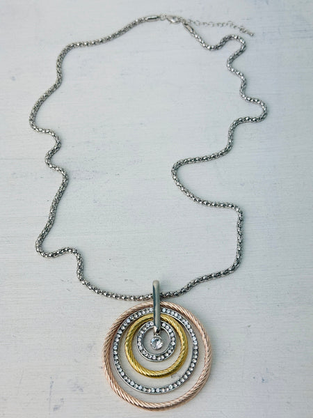 A necklace with three concentric circles in silver, rose gold, and gold colors, featuring a Lobster clasp fastening on a chain.