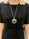 A woman wearing a black dress is modeling a necklace with three circular pendants in silver, rose gold, and gold colors, attached to a chain with a lobster clasp fastening and an extender.