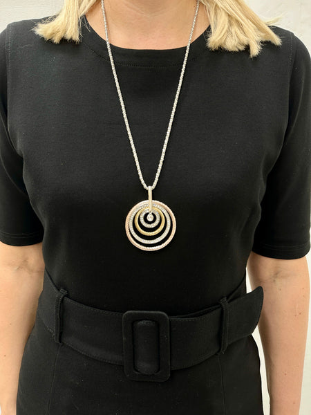 A woman wearing a black dress is modeling a necklace with three circular pendants in silver, rose gold, and gold colors, attached to a chain with a lobster clasp fastening and an extender.