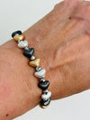 Tri-tone metallic beaded elastic bracelet in gold, silver and dark grey tones with grey spacer beads, displayed on a model.