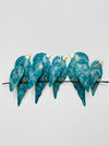 A group of hand-painted metal birds in varying shades of turquoise perched on a horizontal bar.