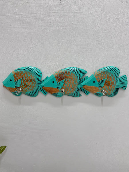 Three turquoise and gold decorative fish wall hooks mounted on a white textured wall.