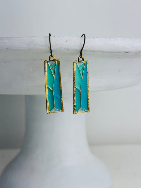 front view of turquoise rectangular earrings with gold accents on a white cake stand.