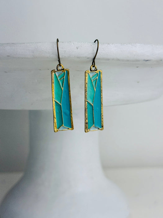 front view of turquoise rectangular earrings with gold accents on a white cake stand.