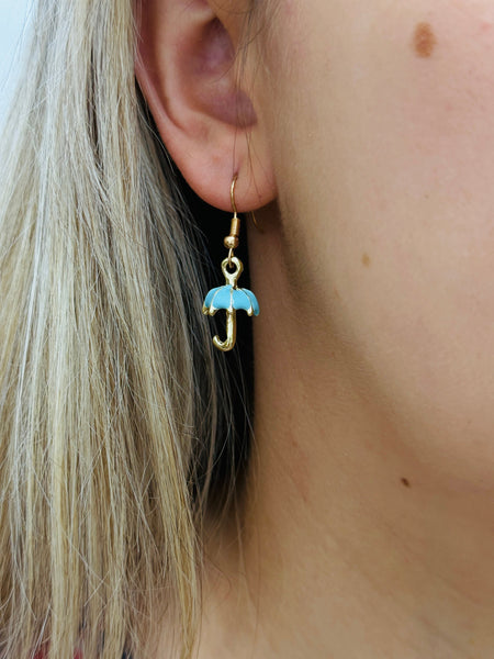Gold earring with a blue umbrella charm worn by a person with blonde hair.