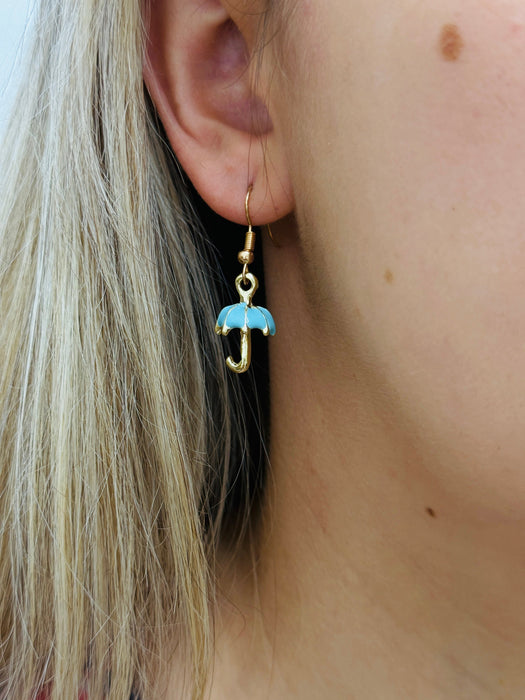 Gold earring with a blue umbrella charm worn by a person with blonde hair.