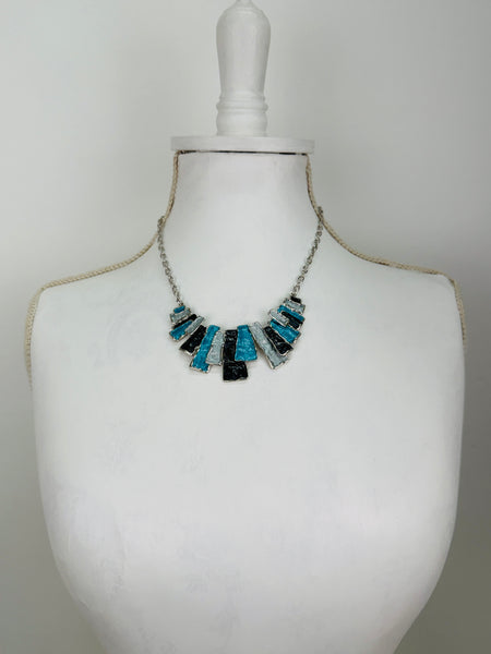 Geometric enamel necklace with layered rectangular pieces in turquoise, grey and gunmetal, on silver-tone chain beads, on a mannequin bust