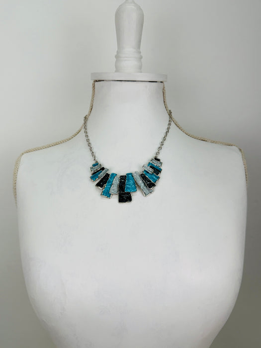 Geometric enamel necklace with layered rectangular pieces in turquoise, grey and gunmetal, on silver-tone chain beads, on a mannequin bust