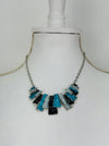 Necklace with turquoise, grey and gunmetal geometric pieces on a silver-tone chain, on a mannequin 