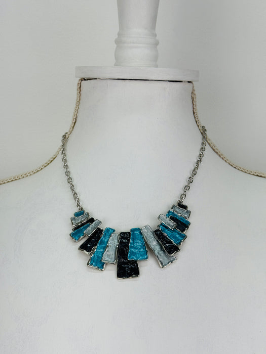 Necklace with turquoise, grey and gunmetal geometric pieces on a silver-tone chain, on a mannequin 