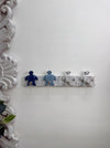 A decorative wall-mounted rack with four small turtle figurine-like hooks in blue, light blue, white, and gray, shown against a white wall with an ornate white frame on the left.