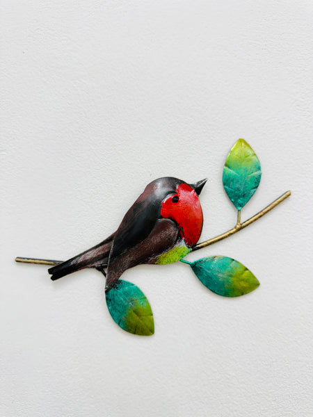 Hand-painted metal robin on a twig with green leaves mounted on a white wall