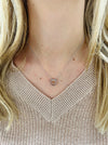 A person wearing a beige knit sweater with a silver double heart necklace.
