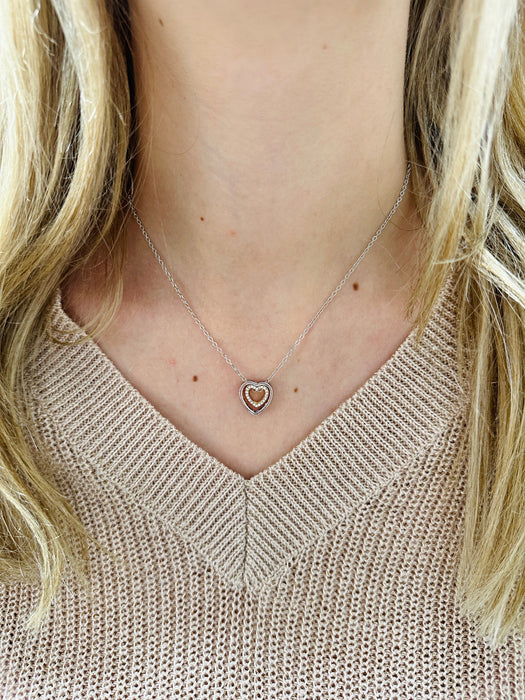 A person wearing a beige knit sweater with a silver double heart necklace.