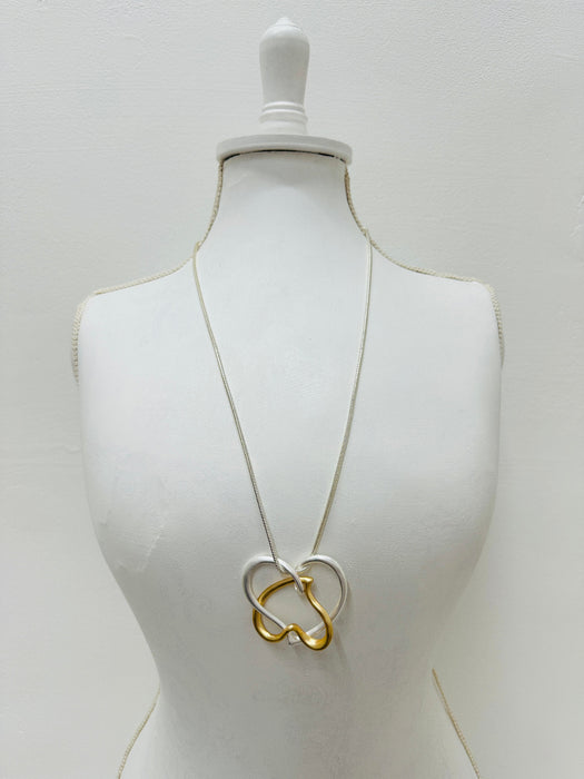 Elegant two - tone intertwined heart pendant necklace on a silver chain displayed on a mannequin