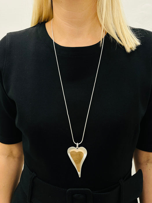 Stylish two - tone long heart pendant necklace on a silver chain displayed on a model