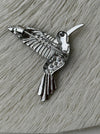 Back view of vibrant hummingbird brooch showing silver-tone metal pin with secure clasp on white textured background