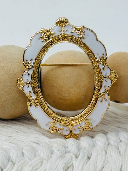 white and gold vintage-style oval frame brooch with ornate detailing