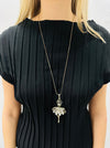 Person wearing a black top with a long necklace featuring a decorative pendant.