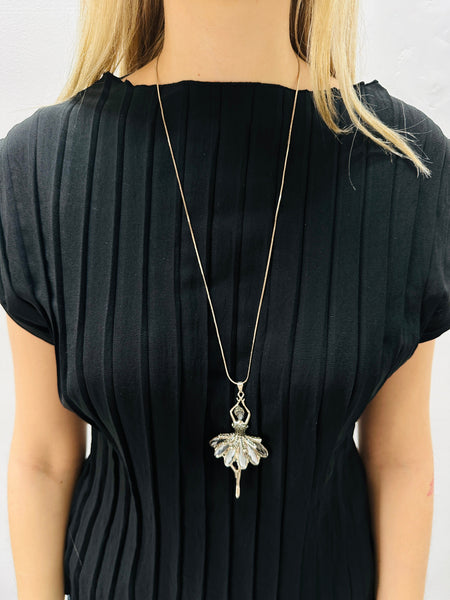 Person wearing a black top with a long necklace featuring a decorative pendant.